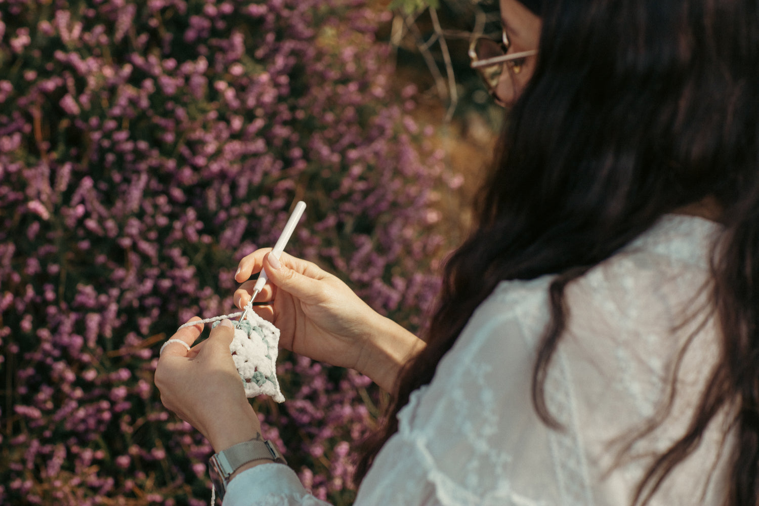 Fille en train de faire du crochet à l'éxtéreir devant des fleurs